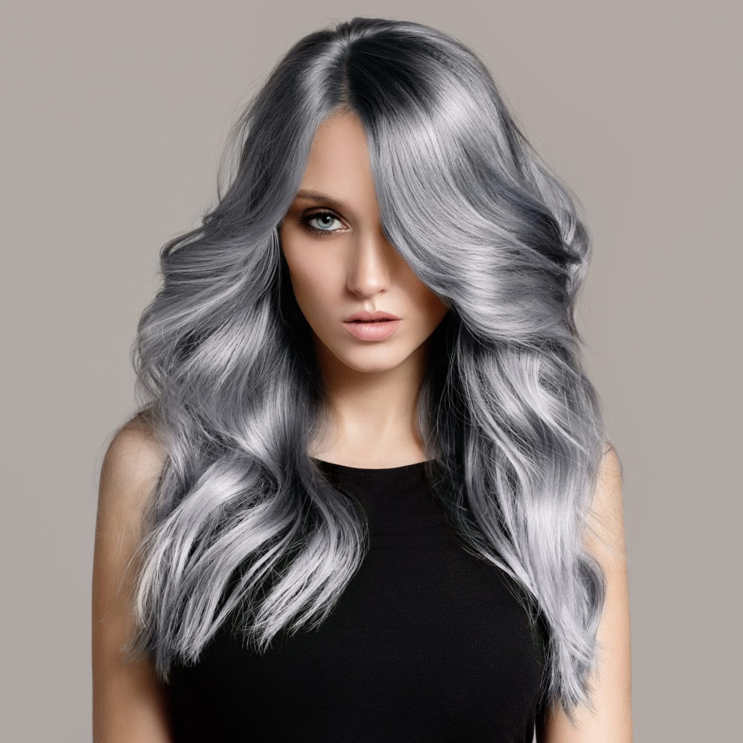 Beautiful woman with long wavy coloring hair. Flat gray background.