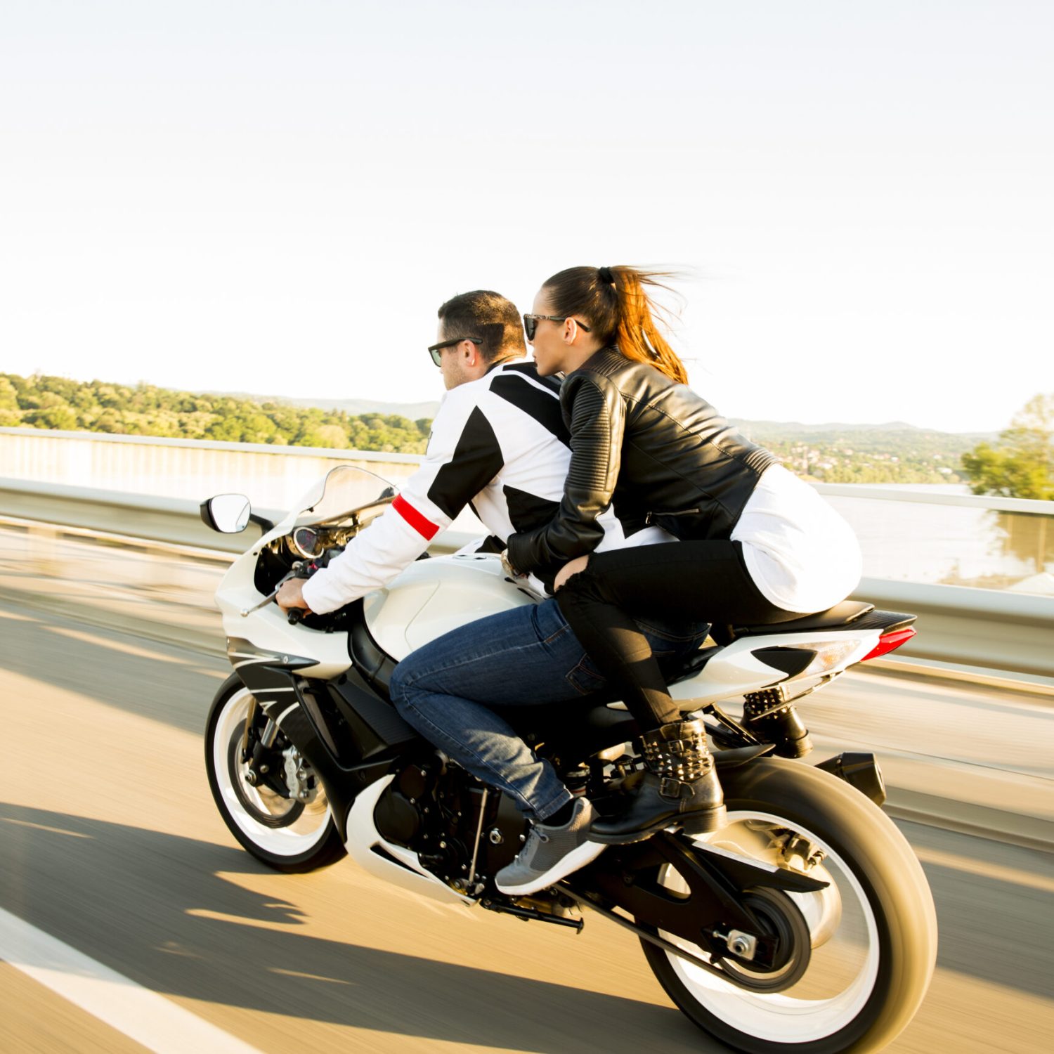 Man and woman wearing leather jackets and stylish sunglasses riding on motorcycle